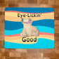 A mousepad with a realistic cartoon style illustration of a crested gecko, sitting down, looking forward while licking one eye with the caption, "Eye Lickin' Good" on a colorful background, the pun and the art are created by Amphisbaena Exotics