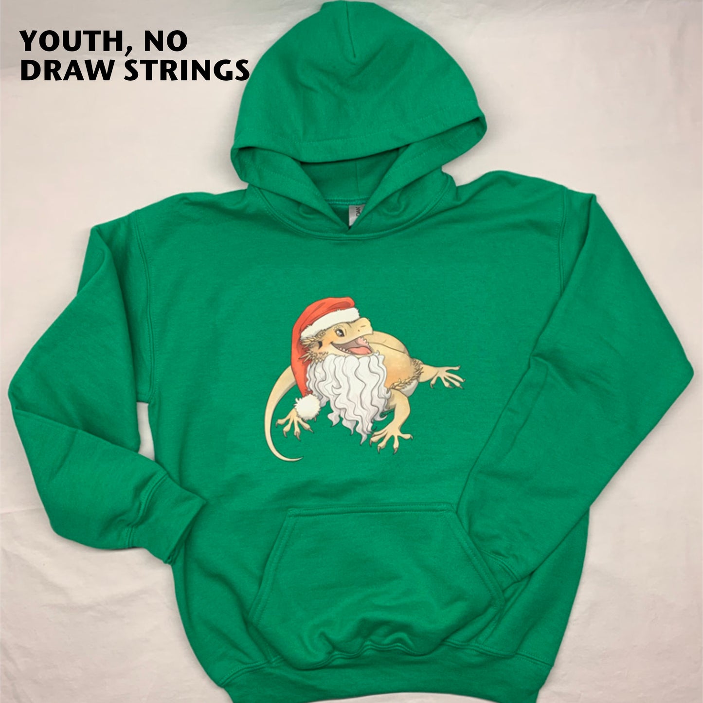 A photo of Amphisbaena Exotics original art of a cartoon realistic bearded dragon, smiling and wearing a Santa hat and beard on a Kelly green pullover hoodie, showing that the youth sizes do not have drawstrings in the hoodie. Christmas themed.
